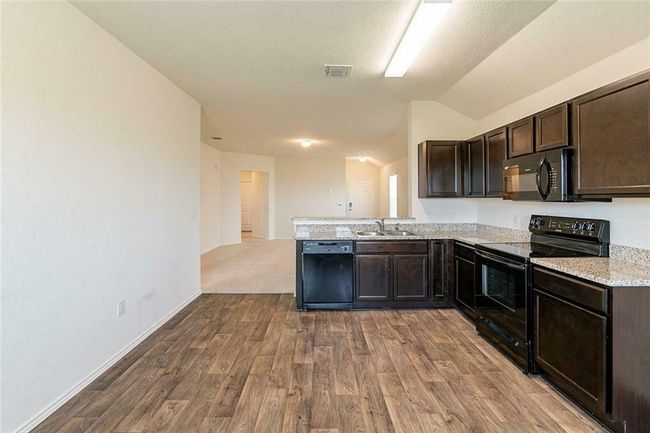 Kitchen featuring black appliances, vaulted ceiling, dark brown cabinetry, wood finished floors, and a peninsula | Image 7