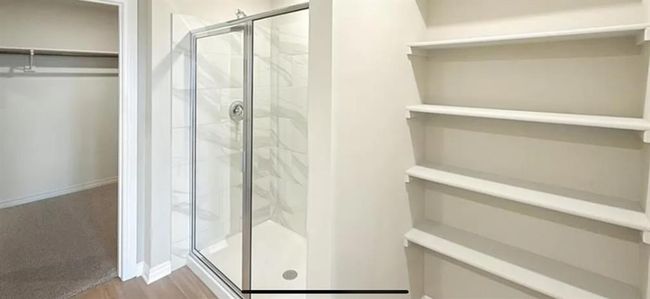 Full bath featuring a marble finish shower, baseboards, wood finished floors, and a spacious closet | Image 12