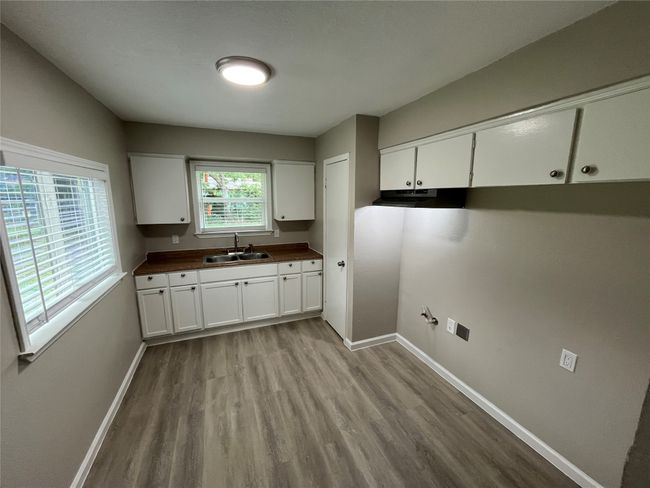 Kitchen with a sink, wood finished floors, baseboards, under cabinet range hood, and white cabinets | Image 6