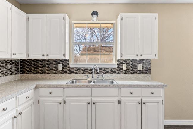Kitchen with light countertops, backsplash, a sink, and white cabinets | Image 12