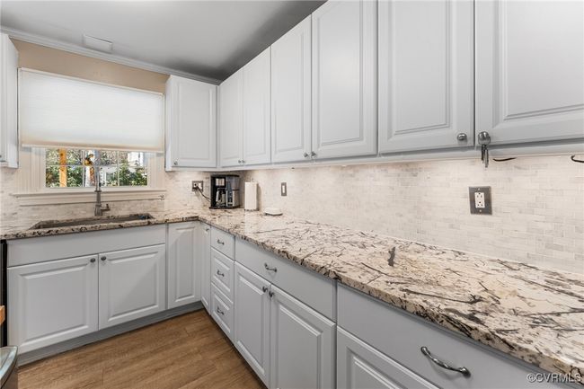 Kitchen with a sink, light stone counters, wood finished floors, white cabinets, and decorative backsplash | Image 12
