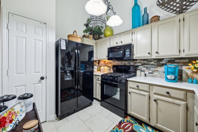 Kitchen with black appliances, light tile patterned floors, light countertops, and decorative backsplash | Image 12