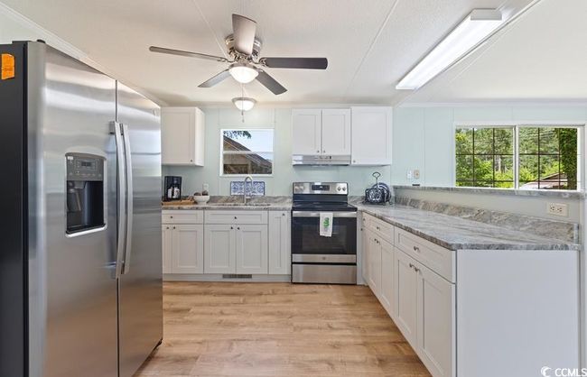 Kitchen with stainless steel appliances, a sink, under cabinet range hood, white cabinetry, and healthy amount of natural light | Image 15