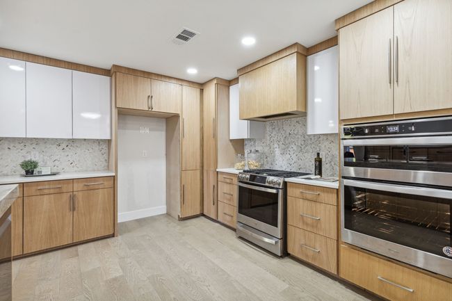 Kitchen with light wood finished floors, visible vents, light countertops, appliances with stainless steel finishes, and custom exhaust hood | Image 14