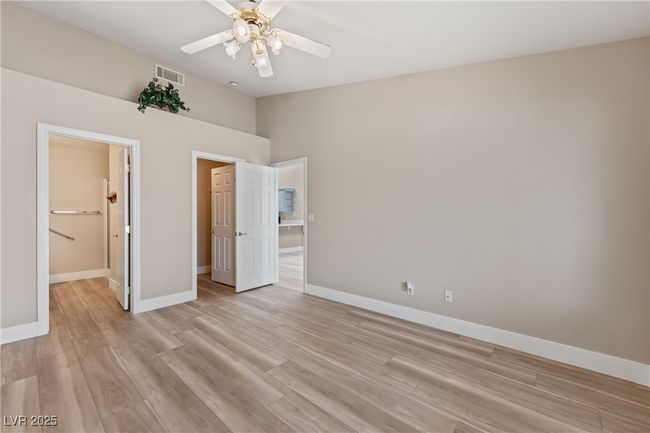 Unfurnished bedroom with light wood finished floors, a walk in closet, ceiling fan, and ensuite bath | Image 22