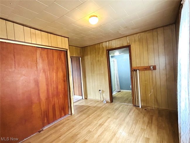 Unfurnished bedroom featuring light wood-style flooring, wood walls, a closet, and baseboards | Image 9