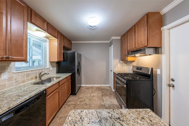 Kitchen featuring stainless steel appliances, backsplash, light stone countertops, ornamental molding, and under cabinet range hood | Image 9