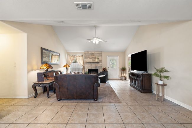 Living area featuring a ceiling fan, light tile patterned floors, baseboards, high vaulted ceiling, and a fireplace | Image 17