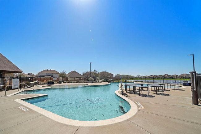 This photo showcases a well-maintained community swimming pool with a spacious deck area, perfect for relaxation and outdoor gatherings. The pool is surrounded by a secure fence and overlooks a scenic neighborhood with clear skies, enhancing the tranquil setting. | Image 25