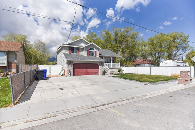 Tri-level home featuring driveway, fence, a porch, brick siding, and a garage | Image 4