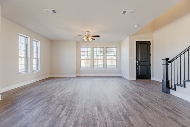 Unfurnished living room with healthy amount of natural light, ceiling fan, stairway, and wood finished floors | Image 7