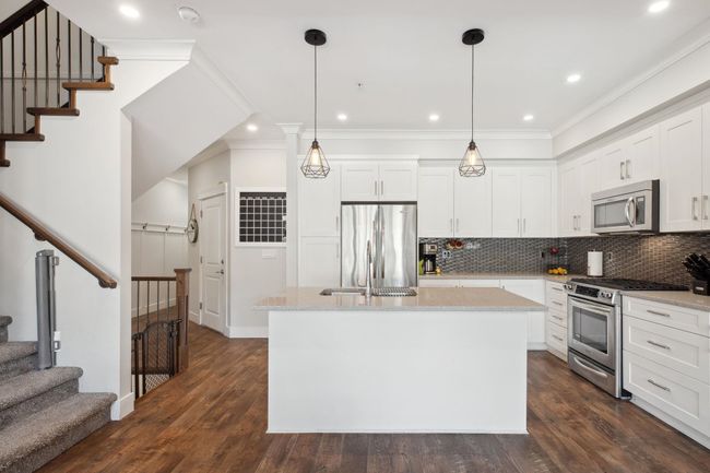 Kitchen featuring white cabinets, a center island with sink, dark wood finished floors, stainless steel appliances, and decorative backsplash | Image 9