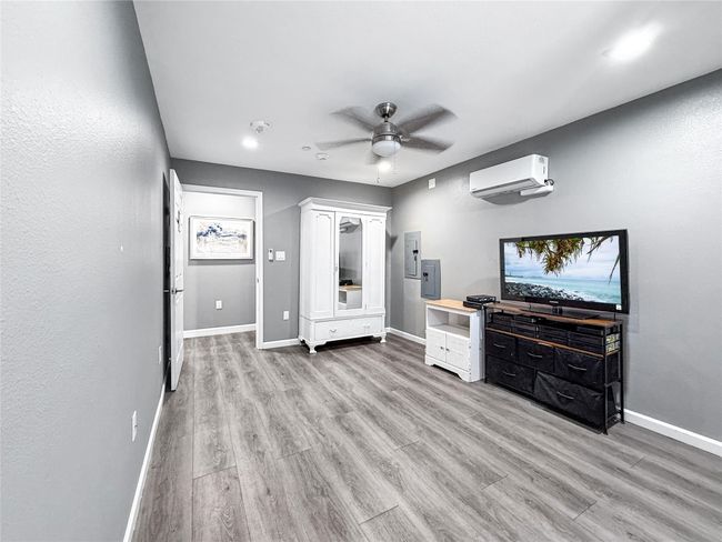 Unfurnished bedroom featuring light wood-style flooring, ceiling fan, electric panel, and an AC wall unit | Image 25