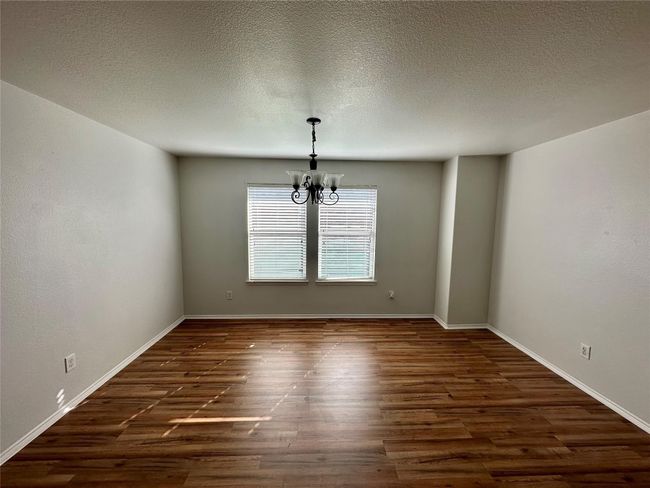 Empty room featuring a textured ceiling, dark wood-style floors, baseboards, and a notable chandelier | Image 7