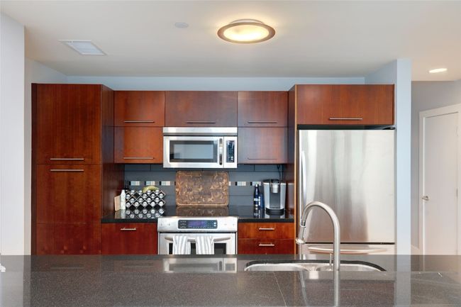 Kitchen featuring stainless steel appliances, modern cabinets, tasteful backsplash, and dark stone countertops | Image 13