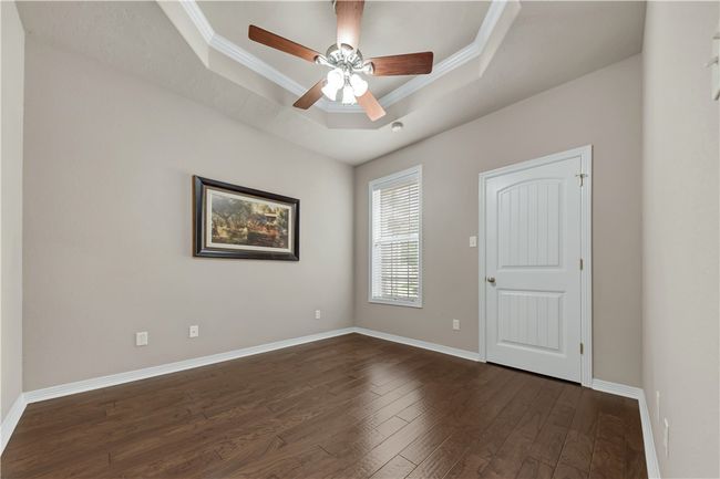 Empty room with a tray ceiling, dark wood finished floors, crown molding, baseboards, and a ceiling fan | Image 28