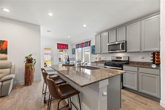 The kitchen features stylish gray cabinets that contrast beautifully with the sleek granite countertops, creating a modern and sophisticated look. A cozy breakfast area is situated by surrounding windows, allowing for plenty of natural light and offering a pleasant spot for casual meals. The back door conveniently leads to the back patio, providing easy access to outdoor dining or relaxation. This kitchen is both functional and inviting, with a layout that seamlessly connects the indoor and outdoor spaces. | Image 8