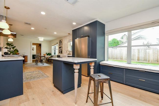 This spacious kitchen features modern navy cabinetry, a central island with seating, and large windows for natural light. It opens into a cozy dining area, perfect for entertaining. | Image 18