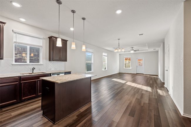 Kitchen with a center island, light granite countertops, hanging light fixtures, decorative backsplash, and sink | Image 14