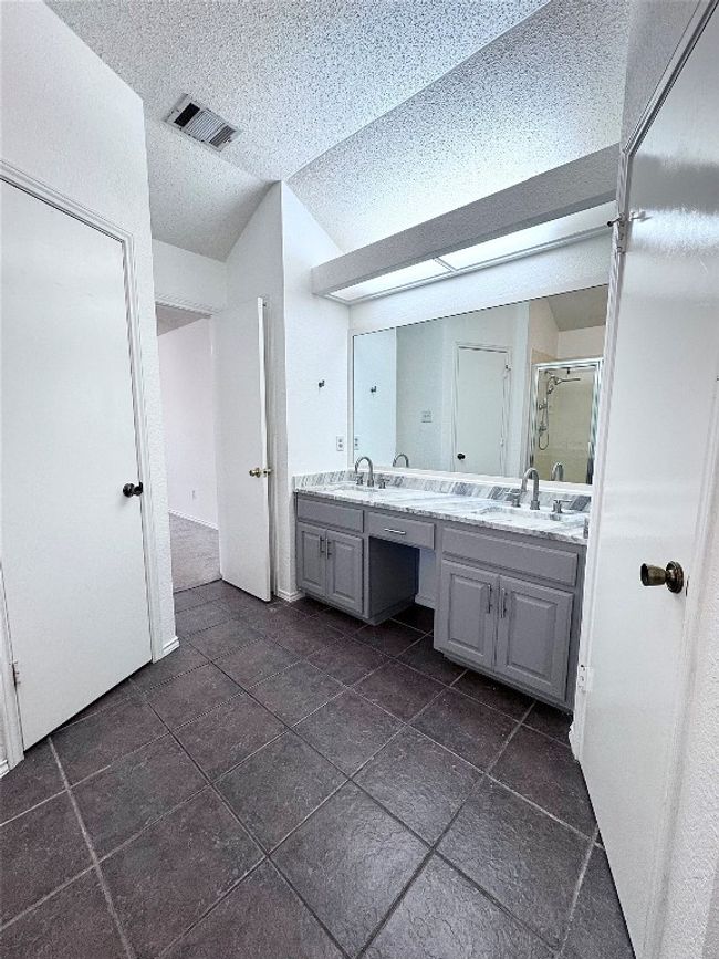 Full bathroom featuring double vanity, a shower stall, a textured ceiling, and lofted ceiling | Image 17