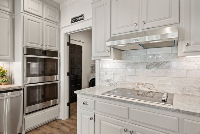 Kitchen with stainless steel appliances, under cabinet range hood, tasteful backsplash, white cabinets, and washer / clothes dryer | Image 19