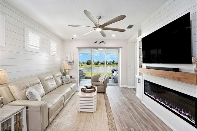 Family room, complete with a postcard-like view of the water view location. Shiplap accent wall and custom built in media/fireplace center with shelves and cabinets for storage. Custom remote screen controls your view and provides shade when needed. | Image 6