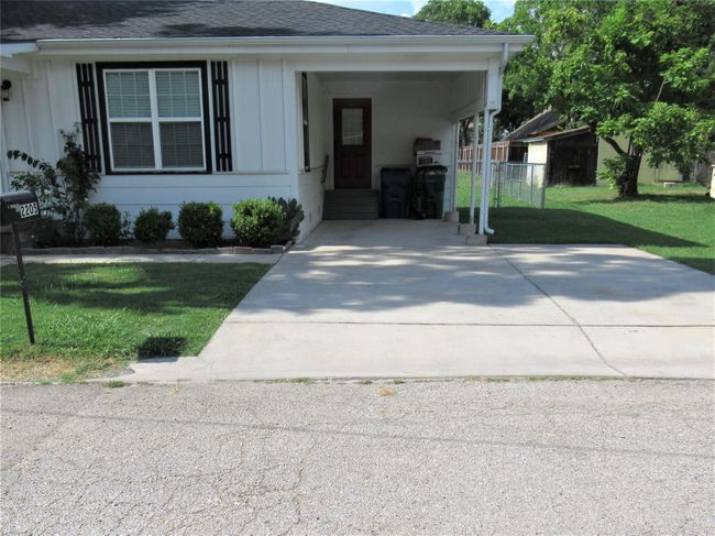 View of front facade with driveway, a front yard, roof with shingles, fence, and a carport | Image 5