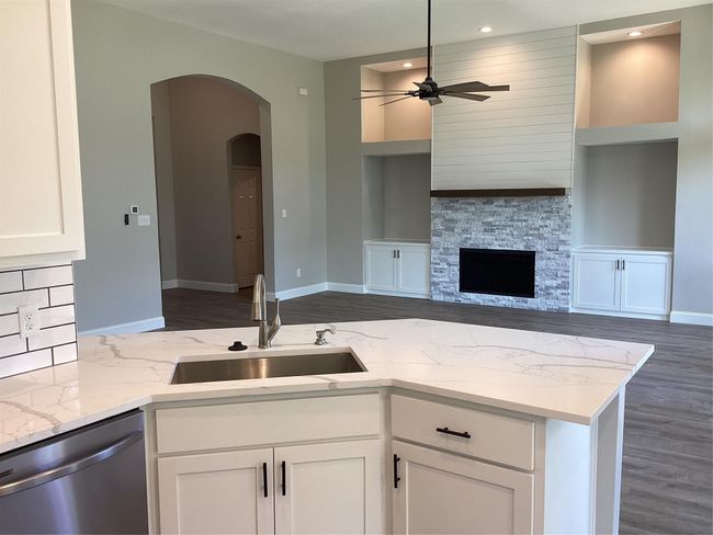 Kitchen featuring stainless steel dishwasher, ceiling fan, arched walkways, light stone countertops, and white cabinets | Image 11