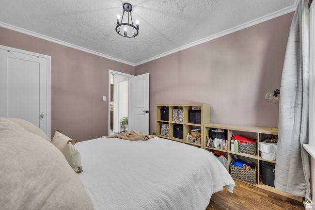 Bedroom with wood finished floors, crown molding, a textured ceiling, and a chandelier | Image 15