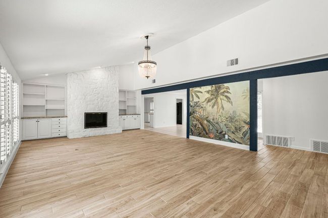 Unfurnished living room with light wood-style floors, a fireplace, built in features, a chandelier, and high vaulted ceiling | Image 7