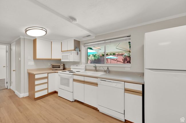 Kitchen featuring white appliances, a sink, light wood finished floors, light countertops, and crown molding | Image 20