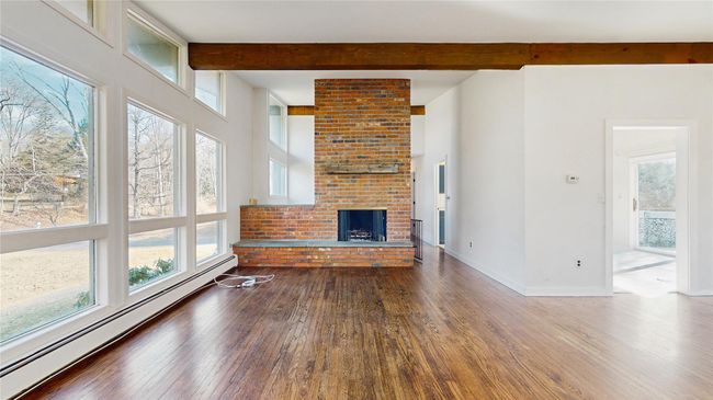 Unfurnished living room with baseboards, beam ceiling, a fireplace, wood-type flooring, and a baseboard heating unit | Image 5