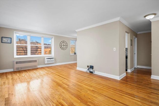 Empty room featuring radiator heating unit, light wood-style floors, ornamental molding, and a wall mounted AC | Image 7