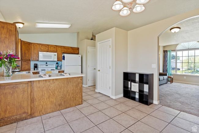 Kitchen with white appliances, a peninsula, a chandelier, vaulted ceiling, and light countertops | Image 9