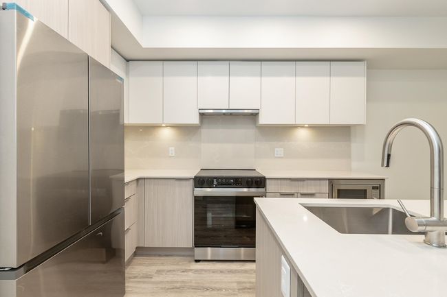 Kitchen featuring freestanding refrigerator, range with electric cooktop, under cabinet range hood, light countertops, and modern cabinets | Image 10