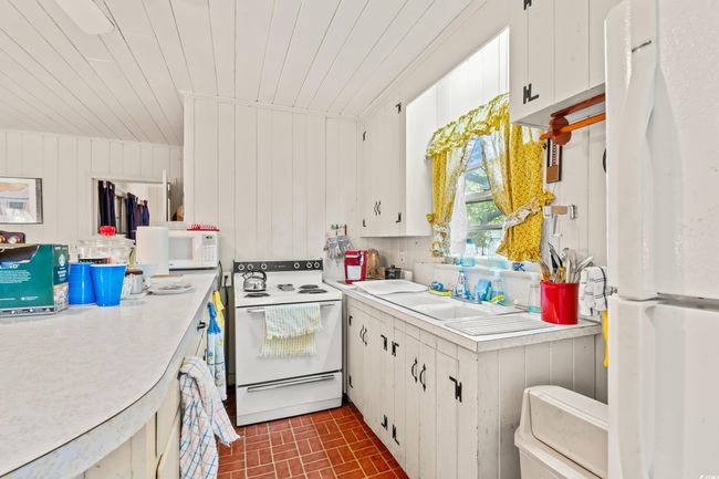 Kitchen with white appliances, brick patterned flooring, light countertops, white cabinets, and wood ceiling | Image 5