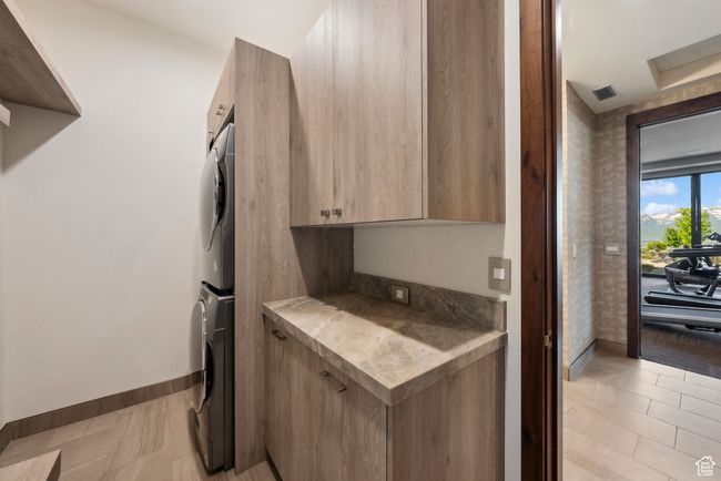 Kitchen featuring estacked washer and dryer, modern cabinets, baseboards, light countertops, and light brown cabinets | Image 81