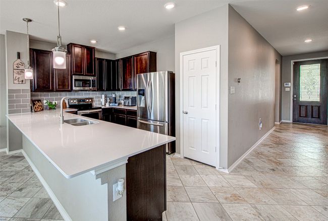 Kitchen with light countertops, a sink, baseboards, decorative backsplash, and appliances with stainless steel finishes | Image 9
