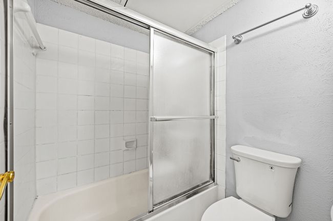 Bathroom featuring toilet, a textured wall, and enclosed tub / shower combo | Image 15