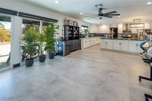Kitchen featuring dark countertops, white cabinetry, appliances with stainless steel finishes, wall chimney exhaust hood, and decorative backsplash | Image 9