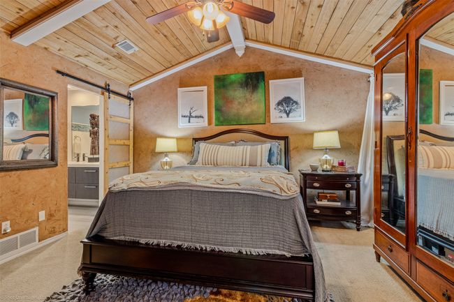 Primary bedroom features a cathedral style wood ceiling, carpeting, ceiling fan, barn door to primary bath | Image 14