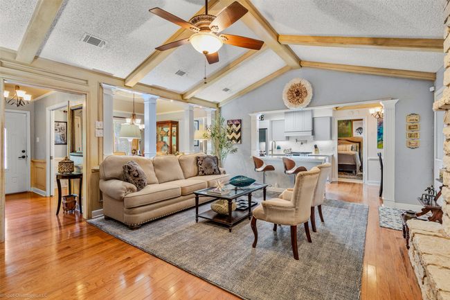 Large living area is conveniently connected with the kitchen and breakfast areas and features, hardwood flooring, a cathedral style ceiling, wood beam accents, a decorative stone fireplace | Image 8