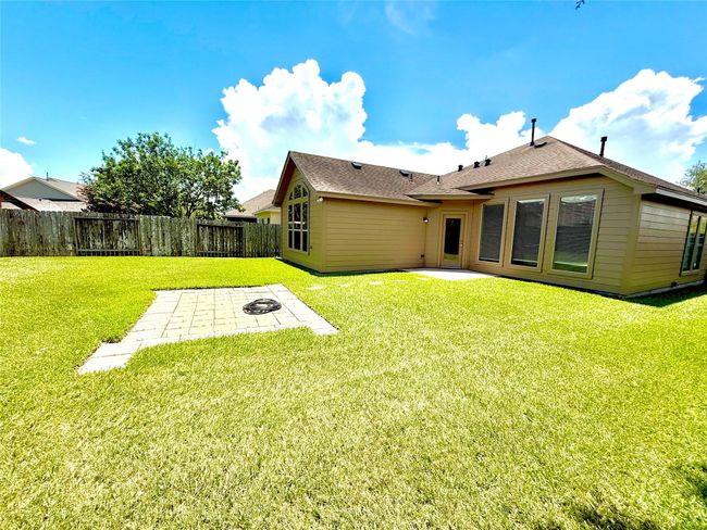This photo showcases a spacious backyard with a well-maintained lawn, a patio area, and a fenced perimeter. The house features large windows and a modern exterior, perfect for outdoor activities and relaxation. | Image 25