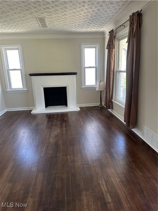 Unfurnished living room with baseboards, visible vents, wood finished floors, and a fireplace with raised hearth | Image 17
