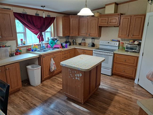 Kitchen featuring white electric range oven, wood finished floors, light countertops, a center island, and decorative light fixtures | Image 4