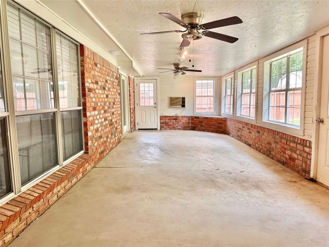 Unfurnished sunroom featuring finished concrete floors, brick wall, a textured ceiling, and a ceiling fan | Image 30