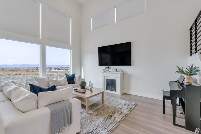Living area featuring light wood-style flooring, a high ceiling, a glass covered fireplace, and baseboards | Image 4