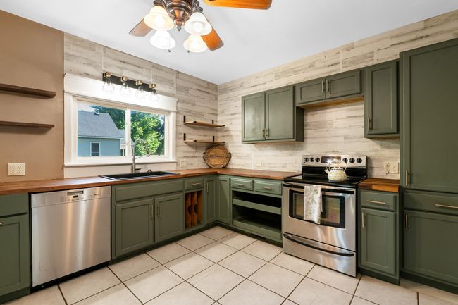 Kitchen with green cabinetry, wooden counters, appliances with stainless steel finishes, and open shelves | Image 10