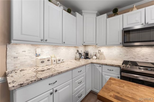 Kitchen with tasteful backsplash, appliances with stainless steel finishes, white cabinetry, and wood counters | Image 11