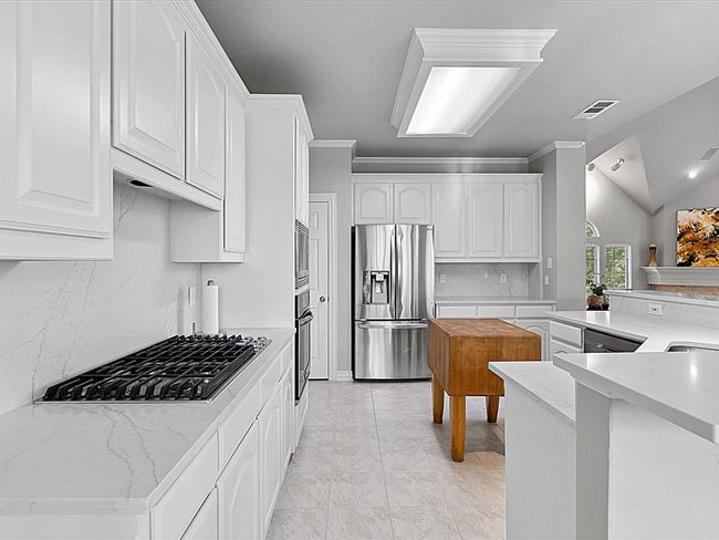 Kitchen featuring backsplash, stainless steel appliances, white cabinetry, vaulted ceiling, and light stone countertops | Image 11